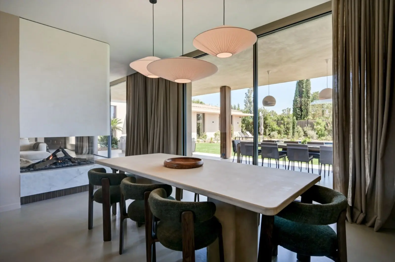 Salle à manger de la Villa F. : table en pierre, chaises en bois foncé et suspensions, ouverte sur le jardin