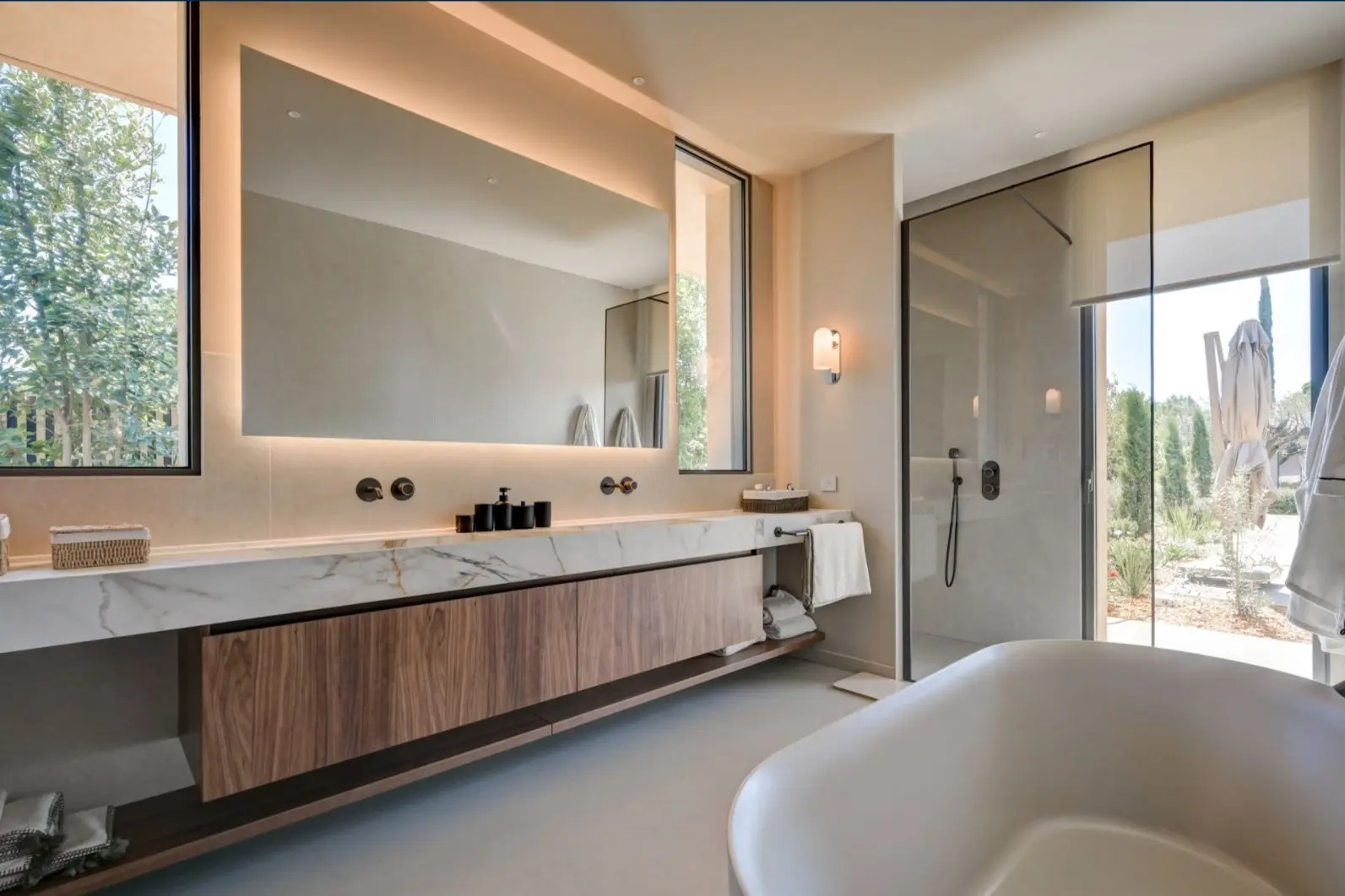 Salle de bain de la Villa F. : meuble vasque en bois, plan en marbre, miroir rétroéclairé et douche vitrée