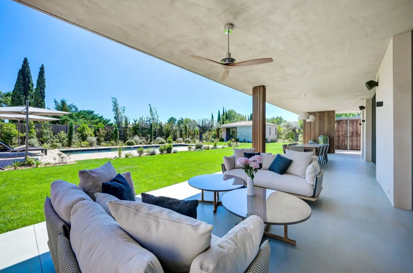 Terrasse couverte de la Villa F. : canapés, table basse et vue sur la piscine et les cyprès