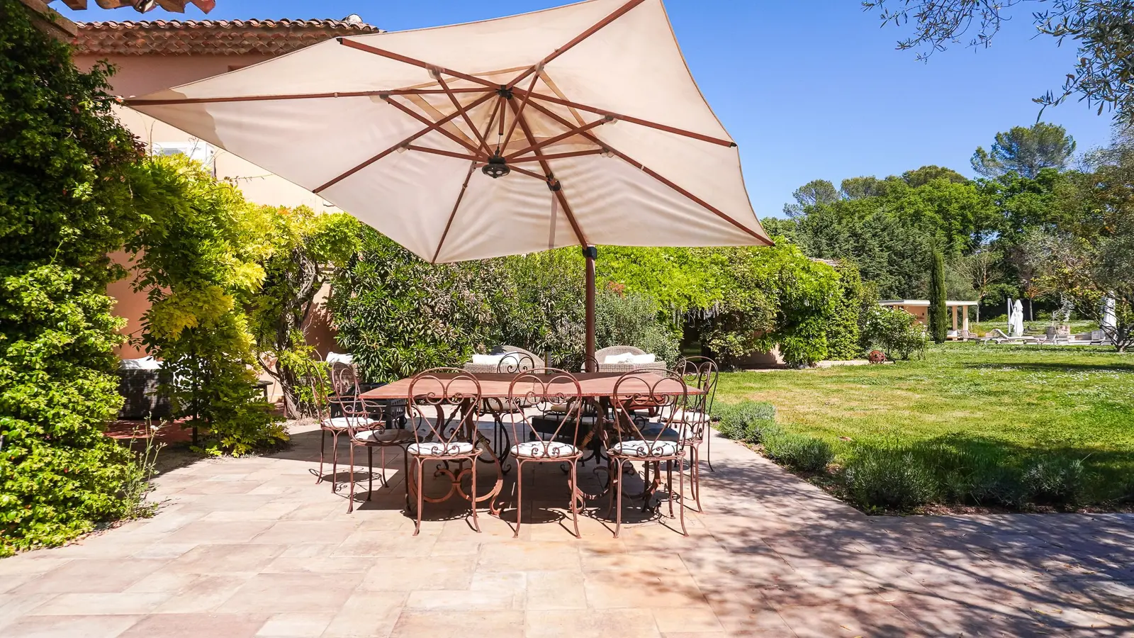 Terrasse en pierre de la Villa S. : grande table sous un parasol, entourée de végétation