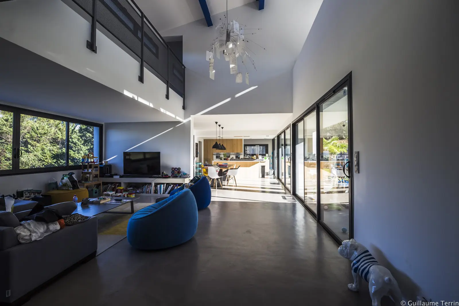 Séjour en double hauteur de la Villa T. : coursive en métal et baies sur le jardin
